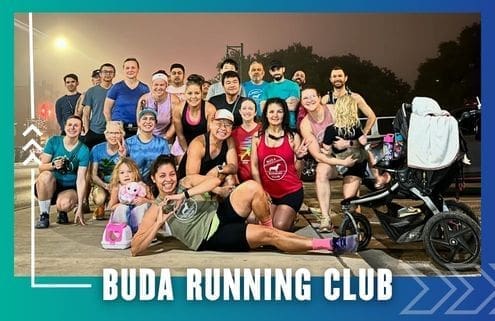 A diverse group of people, including men, women, children, and a stroller, smile and pose together outside at night for a group run under the text "BUDA RUNNING CLUB" with decorative blue and white graphics. Austin Marathon Half Marathon & 5K
