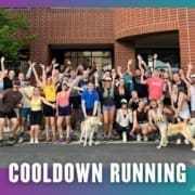 A large, diverse group of people pose together outside a brick building, many smiling and raising their arms after a Group Run. Two dogs are at the front. Text at the bottom reads "COOLDOWN RUNNING." The image is framed with colorful borders. Austin Marathon Half Marathon & 5K