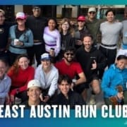 A group of smiling people, dressed in athletic wear, pose together outdoors for a photo. The text at the bottom reads "East Austin Run Club," highlighting a vibrant community running club on a blue and green background with white arrow graphics. Austin Marathon Half Marathon & 5K