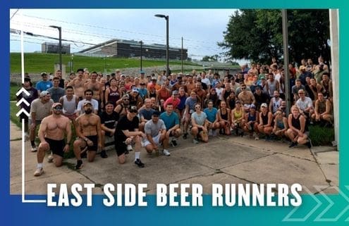 A large group of people in athletic wear pose together outdoors on a paved area, representing the Buda Running Club. "East Side Beer Runners" is written in bold white text at the bottom, with trees and a building visible in the background. Austin Marathon Half Marathon & 5K