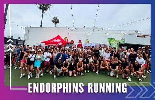 A large group of people in athletic wear pose together outdoors on a sports court under string lights, with a red New Balance tent and surfboards in the background. Text at the bottom reads "ENDORPHINS RUNNING GROUP RUN. Austin Marathon Half Marathon & 5K