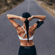 A woman in athletic wear stands on an empty road, adjusting her braided hair as she prepares for a run—a quiet moment of marathon training, where patience is the most underrated skill. Austin Marathon Half Marathon & 5K
