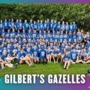 A large group of people wearing matching blue shirts pose for a group photo on grass with trees in the background, representing their running club. Text at the bottom reads "GILBERT'S GAZELLES" with a small gazelle logo on the right. Austin Marathon Half Marathon & 5K