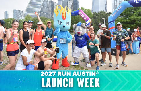 A group of smiling runners pose with two cheerful mascots at the 2027 Run Austin Launch Week event, with city skyscrapers and event banners visible in the background. Austin Marathon Half Marathon & 5K