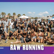 A large group of smiling runners pose together outdoors on grass after a Group Run race, wearing medals and athletic gear, with tents, palm trees, and buildings in the background. Text reads "RAW RUNNING. Austin Marathon Half Marathon & 5K