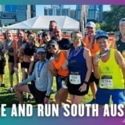 A group of smiling runners from the Buda Running Club, wearing race bibs and medals, pose together outdoors after a group run. A tent and city buildings are visible in the background. Text reads "Rise and Run South Austin. Austin Marathon Half Marathon & 5K