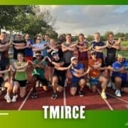 A group of people from the Buda Running Club pose together on a running track, smiling with their arms crossed in front of them. The text "TMIRCE" is at the bottom, featuring a green gradient border and white arrow graphics on the sides. Austin Marathon Half Marathon & 5K