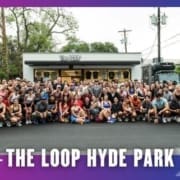 A large group of people, including members of Buda Running Club, pose and smile for a photo in front of The LOOP Hyde Park storefront, with trees and a food truck in the background on a sunny day. Text at the bottom reads "THE LOOP HYDE PARK. Austin Marathon Half Marathon & 5K