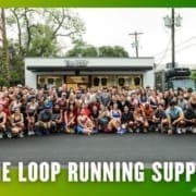 A large group of people, part of a local Running Club, poses in front of The Loop Running Supply store on a street, smiling at the camera. The image has a green and yellow gradient border and text that reads “THE LOOP RUNNING SUPPLY.”. Austin Marathon Half Marathon & 5K