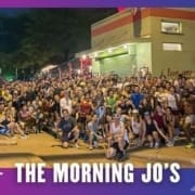 A large, diverse group of people—possibly from a Group Run or the Buda Running Club—poses together outside a building at night under the sign "I love you." Text at the bottom reads "THE MORNING JO’S" on a purple and blue border. Austin Marathon Half Marathon & 5K
