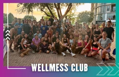 A large group of people pose together outdoors, many smiling and wearing athletic clothes, with trees and buildings in the background. Text at the bottom reads "WELLMESS CLUB" on a colorful border—part of a Buda Running Club group run. Austin Marathon Half Marathon & 5K