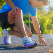 A runner in a blue shirt and black shorts kneels on the road, clutching his painful knee—an all-too-common setback during marathon training—showing that patience is often the most underrated skill for distance athletes. Austin Marathon Half Marathon & 5K